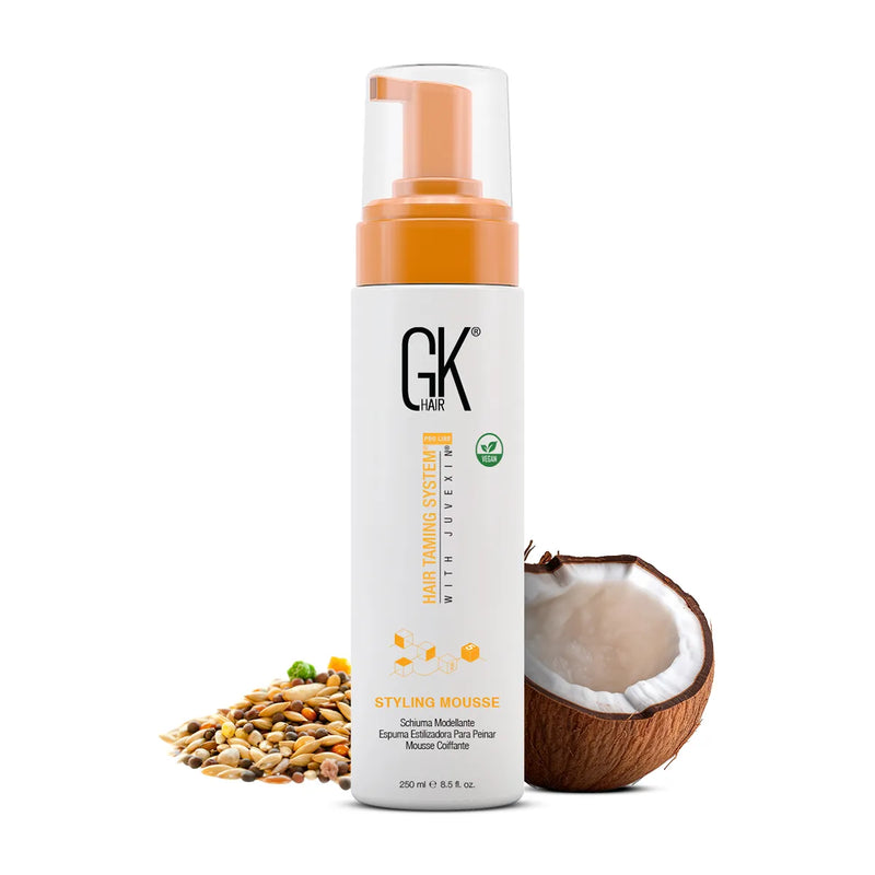 GK Hair Styling Mousse 250 ml white bottle with an orange foamer pump and vegan badge, beside mixed grains and half a coconut
