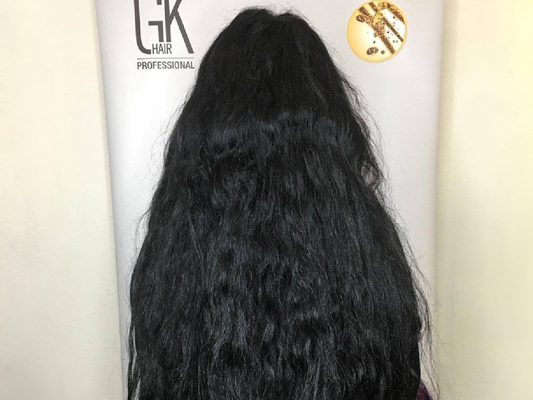 Before: long frizzy wavy black hair from behind against a GK Hair Professional banner